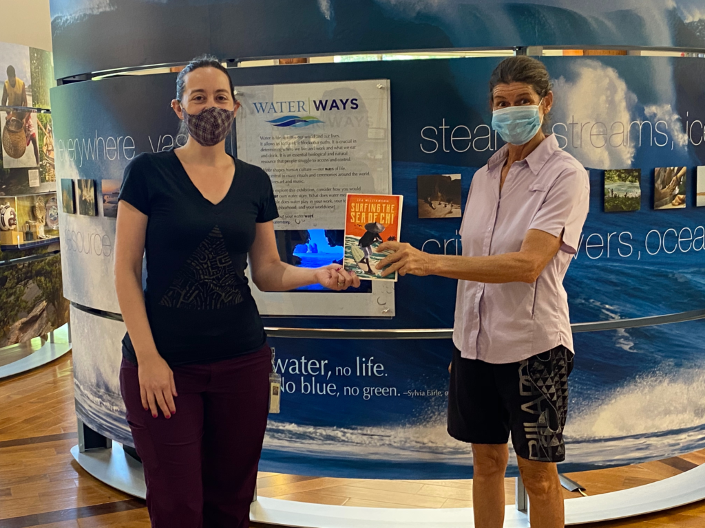 Two people standing in front of a museum exhibition on water/ways holding a book.