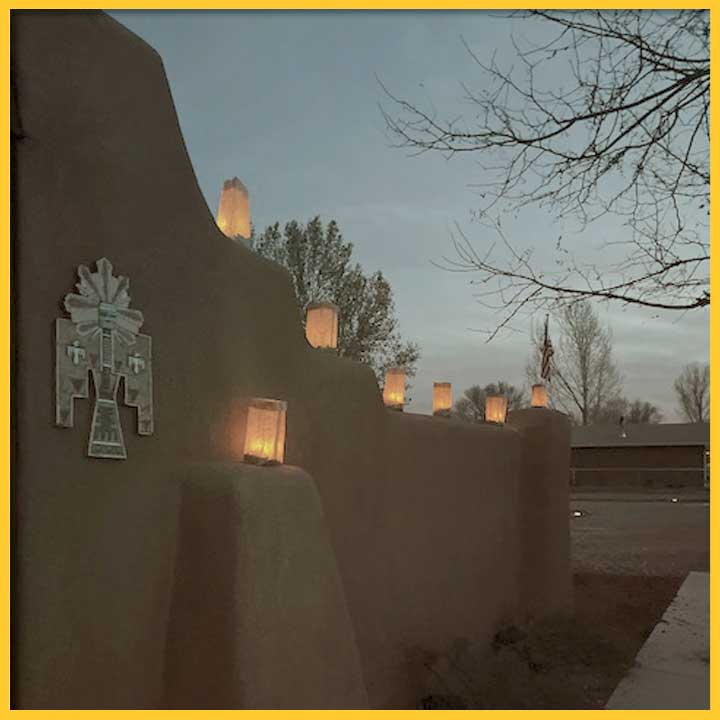 Luminarias (lights in brown paper bags) sit on an adobe wall in New Mexico at dusk. 