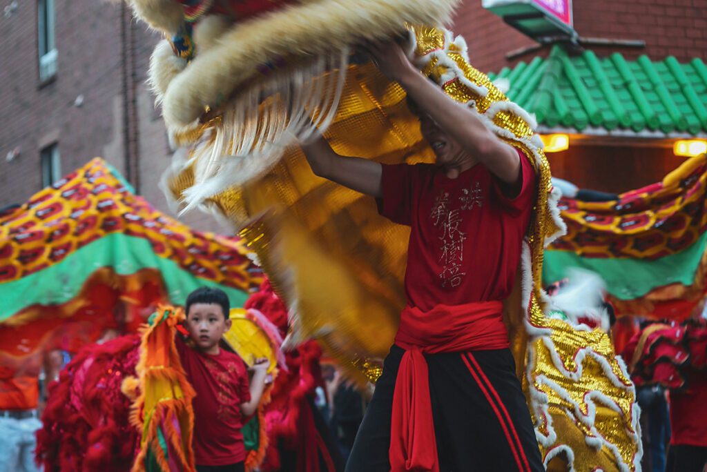 A man and young boy dancing with a large dragon puppet for Chinese new year celebrations. Everyone is wearing red and there are also green and gold fabrics.